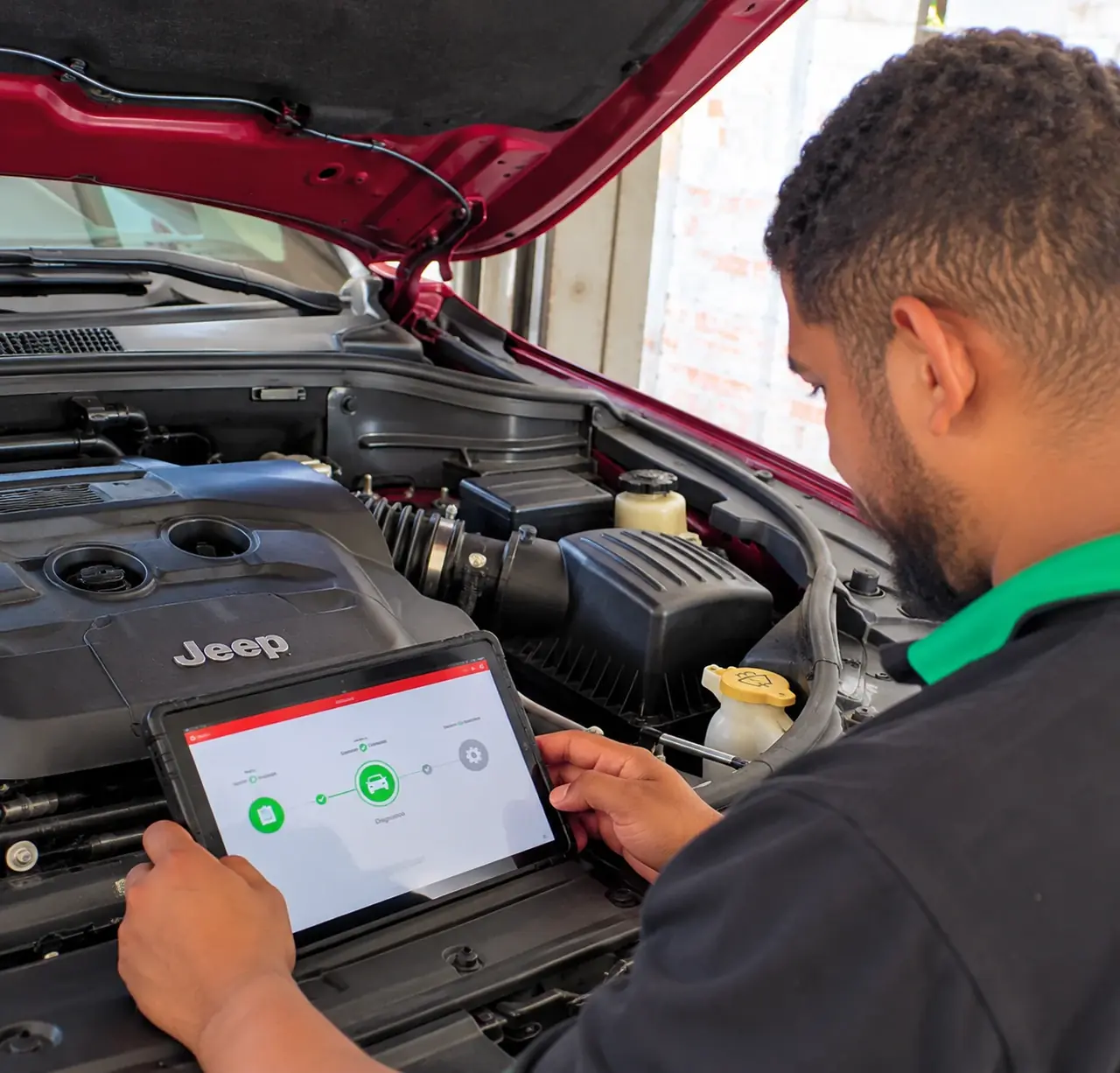 Técnico usando o scanner de diagnóstico em um tablet, diante do motor de um Jeep com o capô aberto.