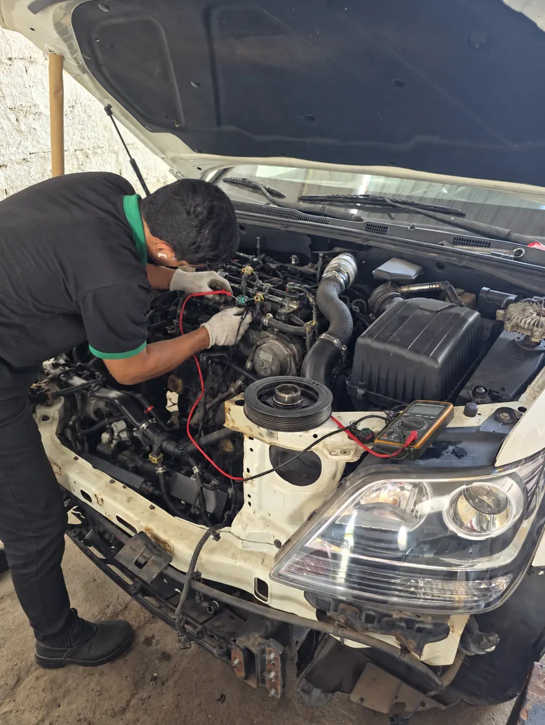 Técnico testando a parte elétrica do motor com um multímetro, com o capô aberto e os cabos de teste conectados.