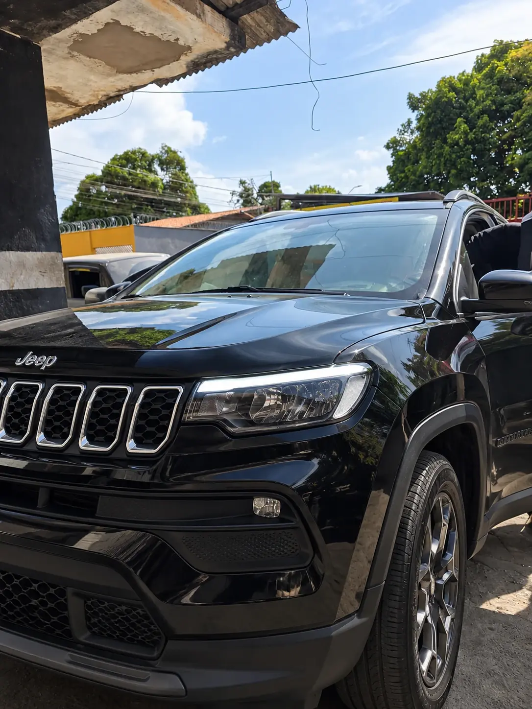 Jeep Compass preto na entrada da oficina, visto de frente pela lateral do motorista.
