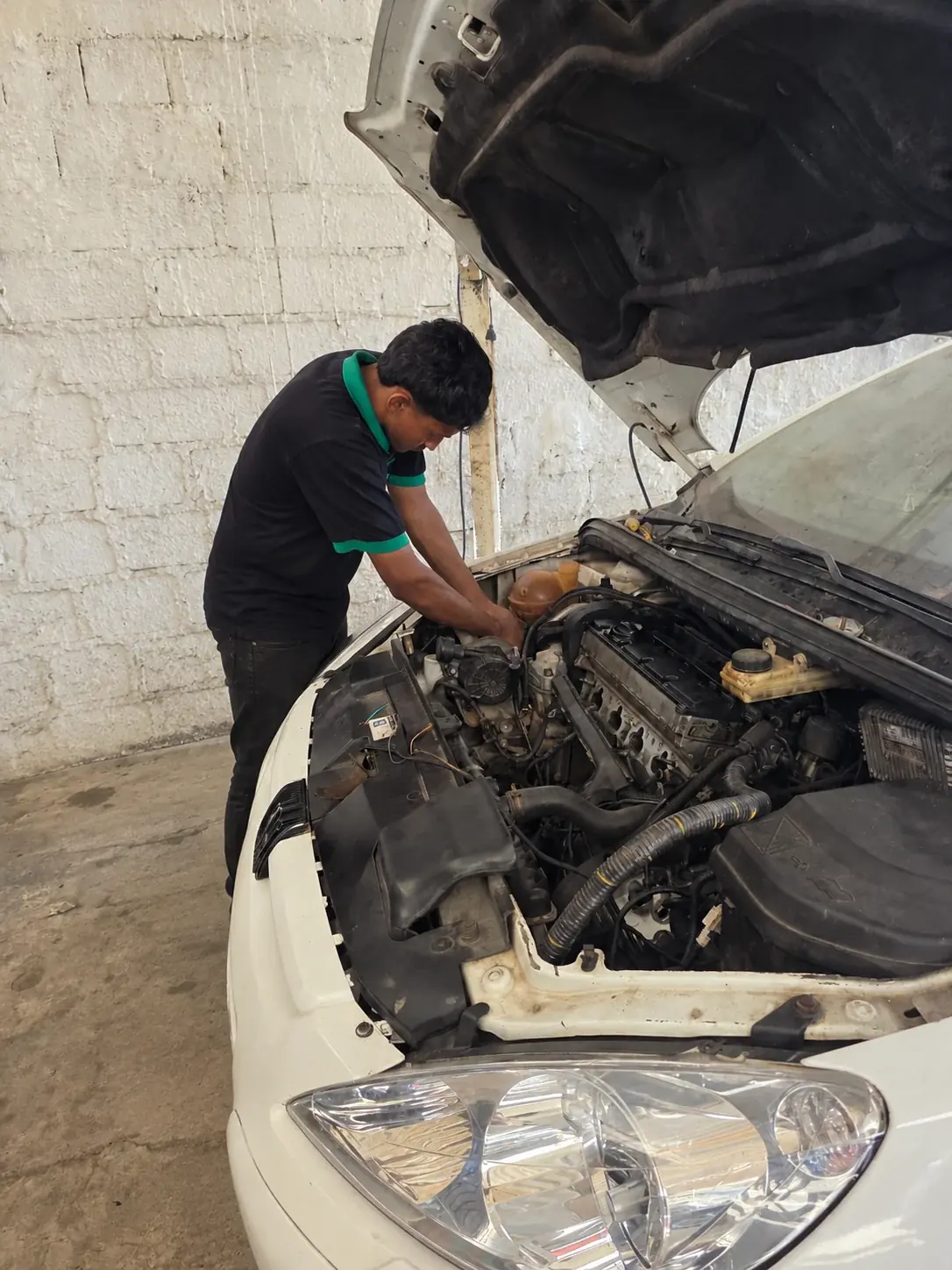Técnico fazendo a manutenção no motor de um carro branco, com o capô aberto, na oficina.