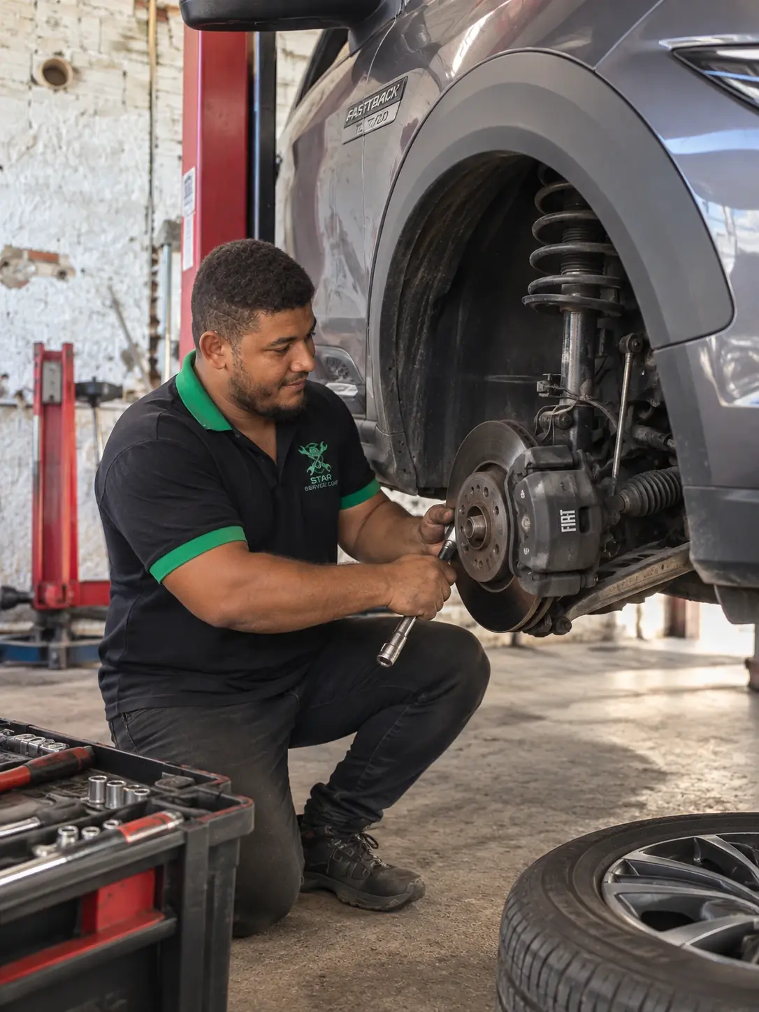 Técnico da Star Service Car inspecionando o disco de freio e a suspensão dianteira de um Fiat Fastback, com a roda removida.